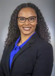 Professional woman in business attire with glasses, smiling confidently.