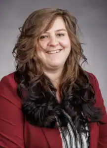Woman with long wavy hair smiling, wearing a red blazer.